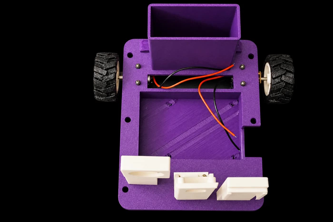 The printed chassis from above, wheels and motors fitted, with the battery bay and the three printed mounts laid out below it