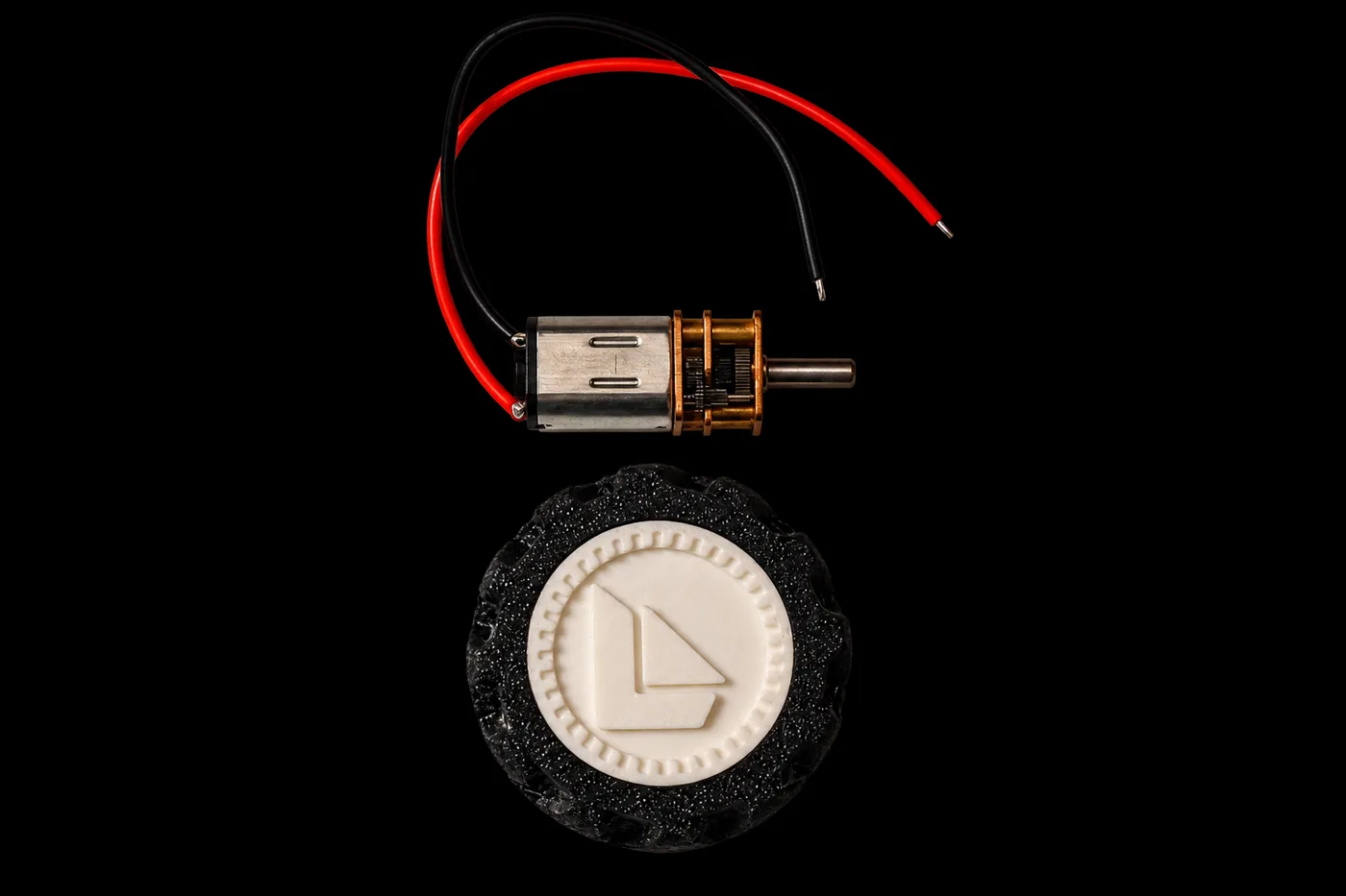 An N20 geared motor with its red and black leads, above one of the treaded wheels